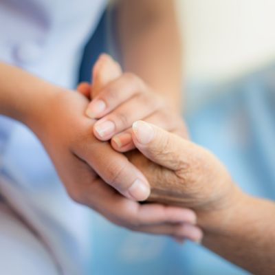 Eine Krankenschwester hält die Hand einer älteren Person und zeigt damit Fürsorge und Unterstützung in einem Pflegekontext.