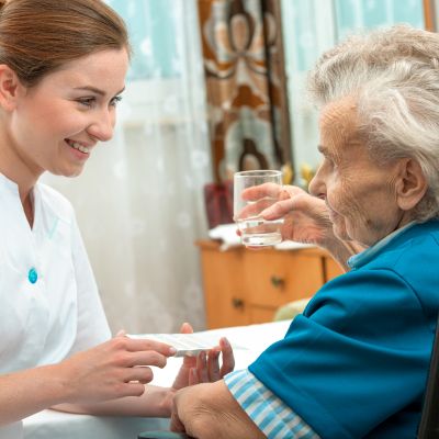 Eine Krankenschwester reicht einer älteren Frau ein Glas Wasser, um ihr bei der Flüssigkeitsaufnahme zu helfen.