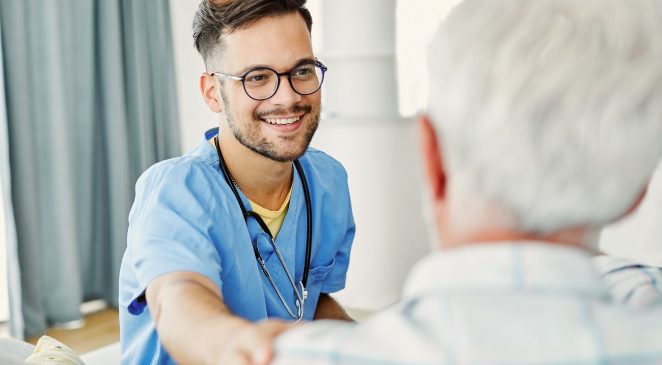 Männliche Pflegefachkraft lächelt einen Patienten an