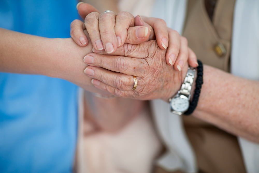 Eine Pflegerin hält die Hand einer alten Patientin.